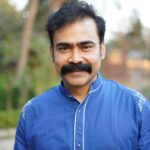 Portrait of a happy man with mustache smiling outdoors in a blue shirt.