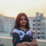 A young woman stands confidently on a rooftop in Dhaka, Bangladesh, during sunset.